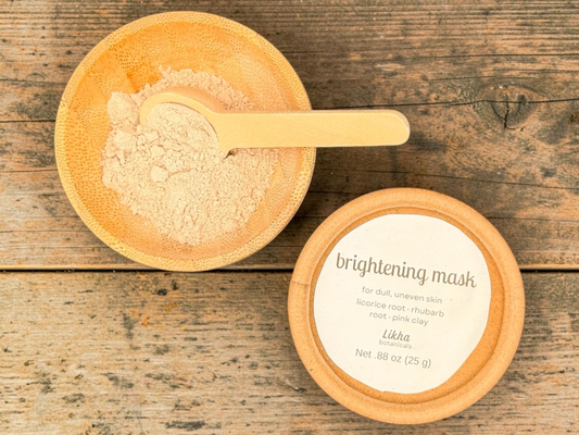 Brightening powdered face mask in round tin with cream-colored powder in wooden bowl and bamboo scoop on rustic wood surface