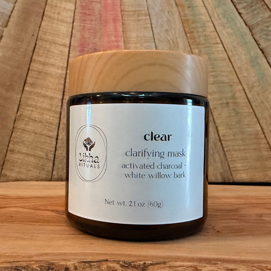 A jar of Likha Rituals 'clear' clarifying mask, featuring a white label and a light-colored wood lid, set against a rustic wooden background.