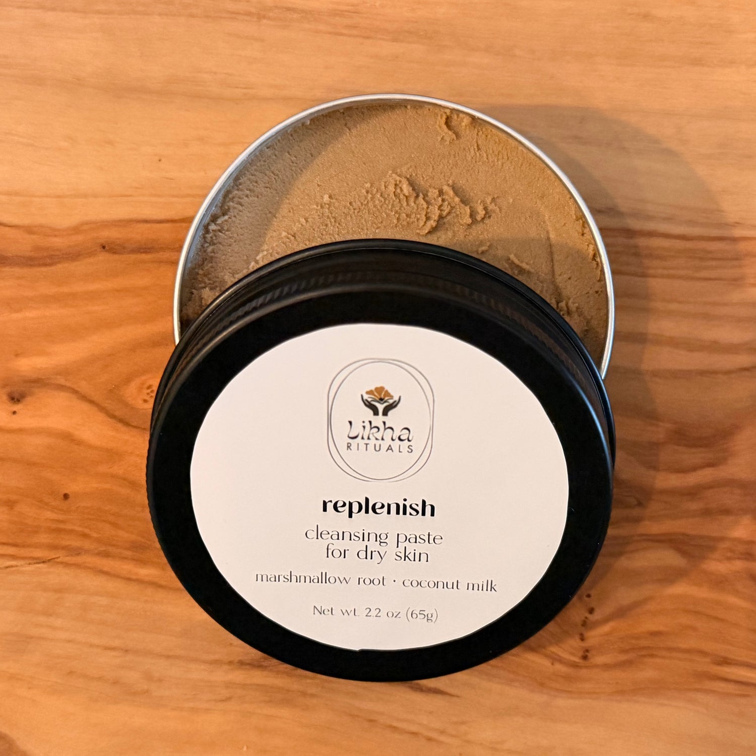 An open round metal tin of Liba Rituals Replenish Cleansing Paste for dry skin, showing the light brown paste inside, placed on a wooden surface.