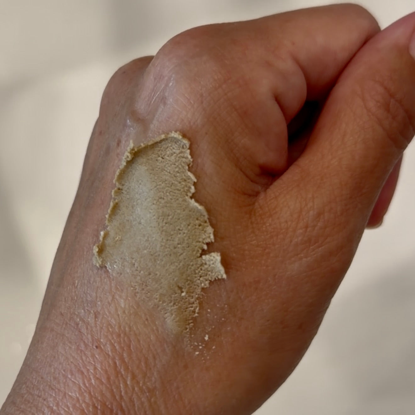 A close-up of a hand showing a textured beige paste application on the back of the hand.